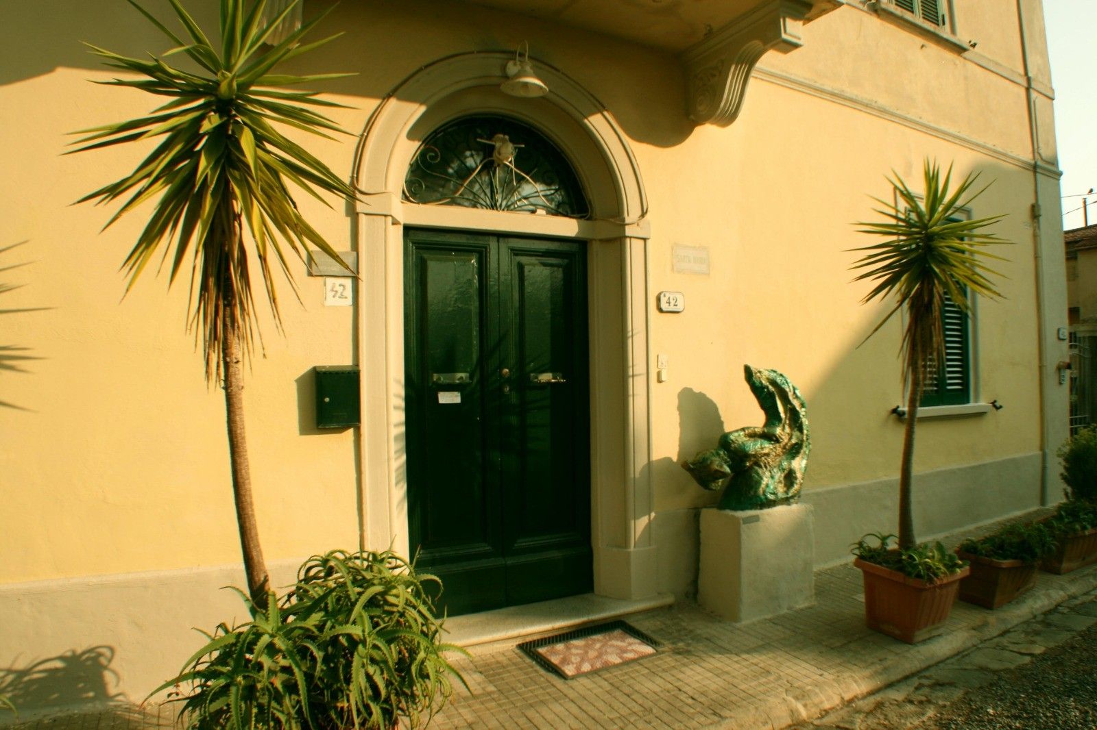 A building with a green door, numbered 42, and a small sculpture on the porch.