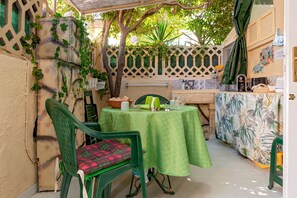A small outdoor dining area with a table and chairs, a basket, and a green umbrella.