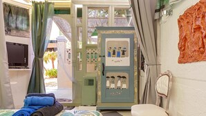 Una habitación con cama, sillón, televisión y refrigerador decorado con obras de arte.