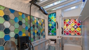Un baño con paredes de mosaicos, un inodoro y una zona de ducha.