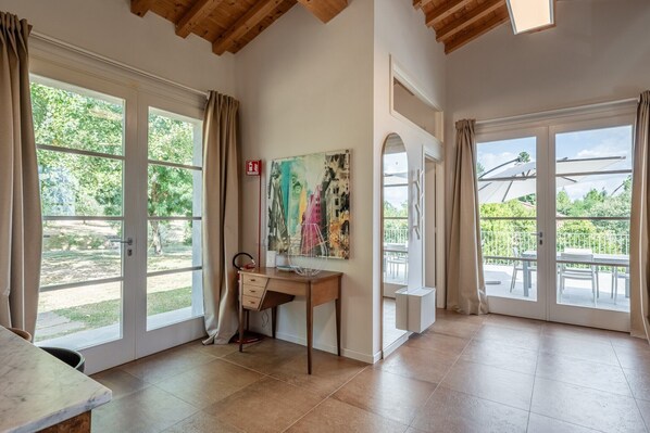 Une pièce avec un bureau, deux grandes fenêtres, un tableau et un balcon.
