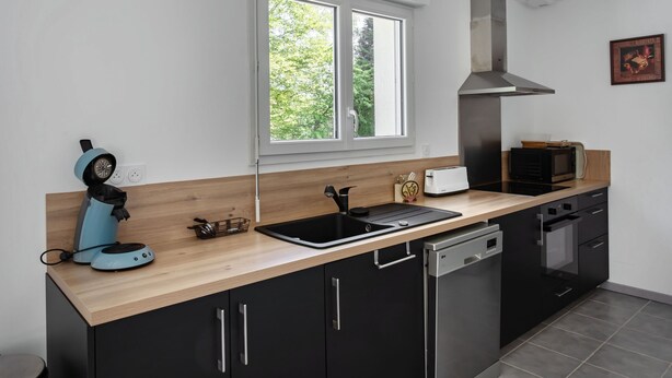 A modern kitchen with a built-in dishwasher, a microwave, a toaster, and a window with a view of trees.