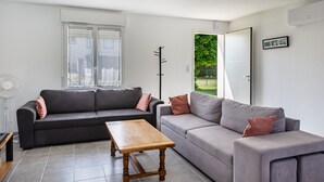A modern living room with two sofas, a wooden coffee table, a standing fan, and a large window.
