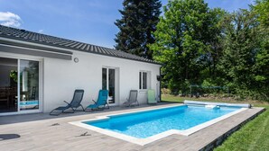 A modern house with a swimming pool, a covered patio, and a lawn.