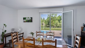 A dining area with a table set for four, wooden chairs, a potted plant, and a painting on the wall.