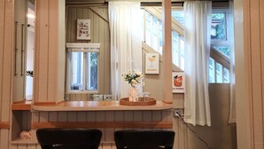 Eine Küche mit einer Holzausziehtafel, zwei schwarzen Stühlen, einer Blumenvase und einem Fenster mit Vorhängen.