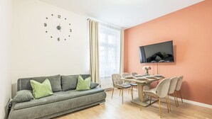 A modern living room with a grey sofa, a dining table with chairs, a TV mounted on the wall, and a large window with curtains. - Washington by Interhome (Prague centre)