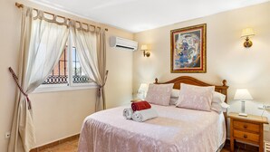 Un dormitorio con cama, cortinas, un cuadro, dos lámparas de noche y una mesita de noche.