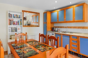 A modern kitchen with blue cabinets, a dining table with chairs, a bookshelf, and a microwave. - Apartment 'Con Encanto' with Sea Views, Wi-Fi and Air Conditioning (Las Lagunas de Mijas)