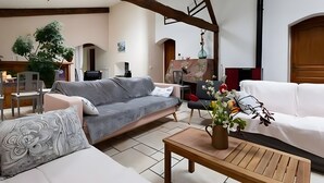 A living room with a grey sofa, white sofa, and a wooden coffee table. There is a potted plant and a vase with flowers on the coffee table. - Guest Room “Chambre Ancolie” – Private Terrace, Shared Garden, Wi-Fi, E-Bike Friendly (L'Épine)