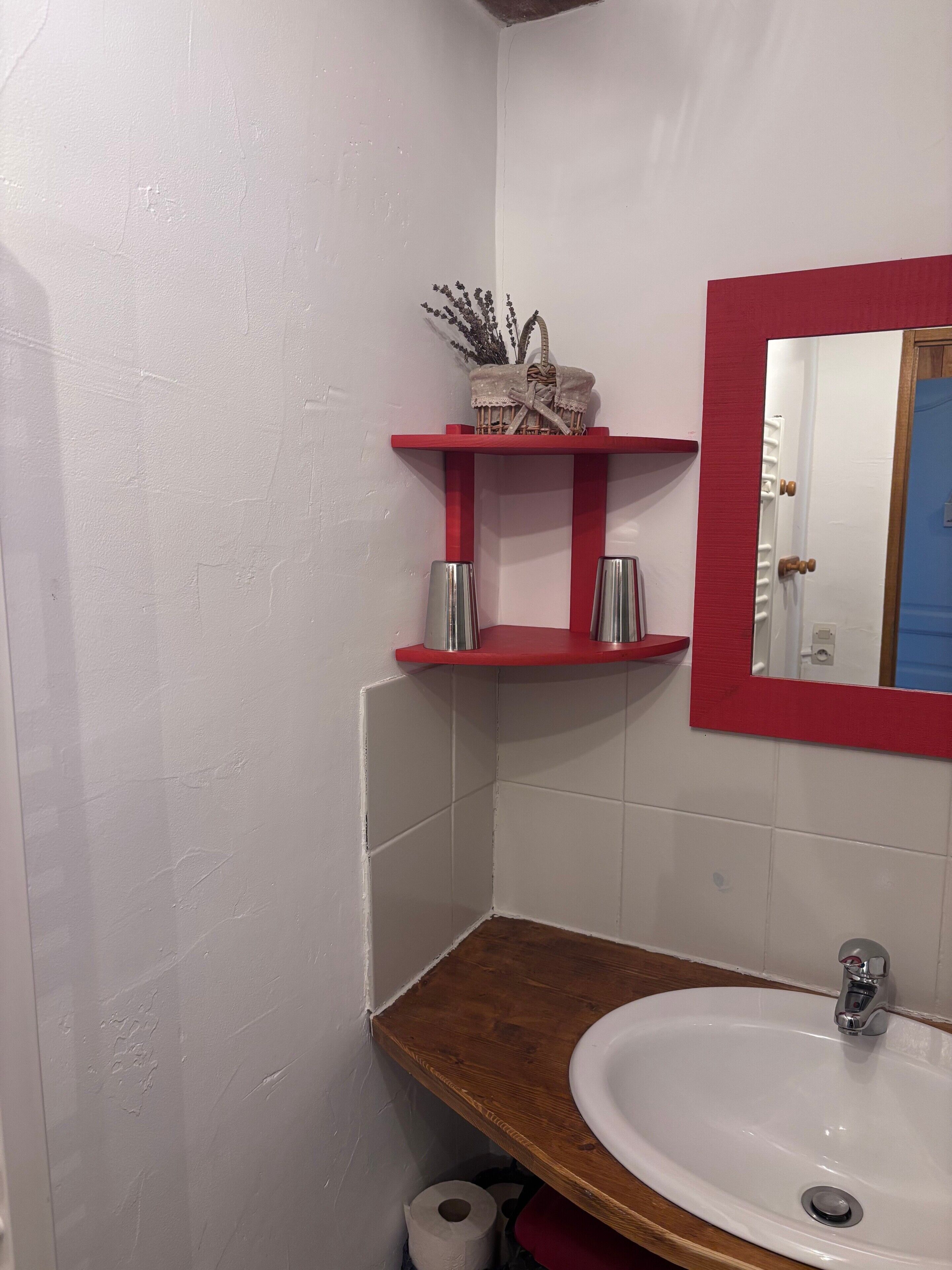 A bathroom with a white sink, red shelves, a mirror, and a wooden countertop.