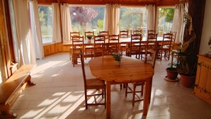 A wooden dining room with a large table and chairs, potted plants, and a view of trees through the windows. - "Cytise" Room with Private Terrace, Shared Garden, Wi-Fi, E-Bike Friendly (L'Épine)