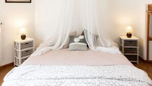 Een slaapkamer met een hemelbed, nachtkastjes met lampen, een ingelijst schilderij aan de muur en een houten plafond.