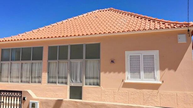 Un bâtiment avec un toit recouvert de tuiles, de grandes fenêtres avec des rideaux et une petite porte.