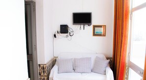 A white sofa with patterned cushions, a flat-screen TV mounted on the wall, and a framed picture above the TV.