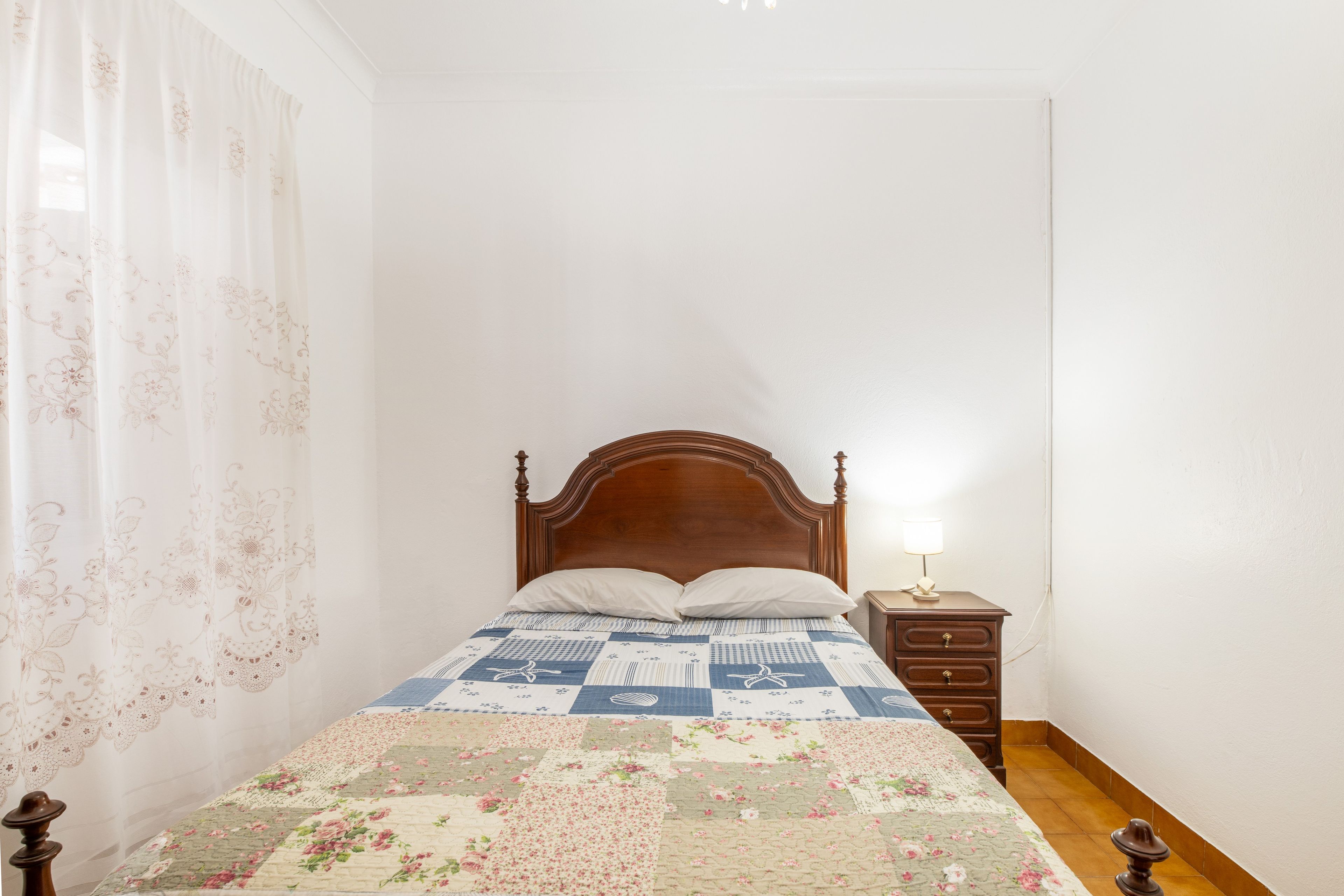 A bedroom with a wooden bed, a nightstand with a lamp, and a floral quilt.