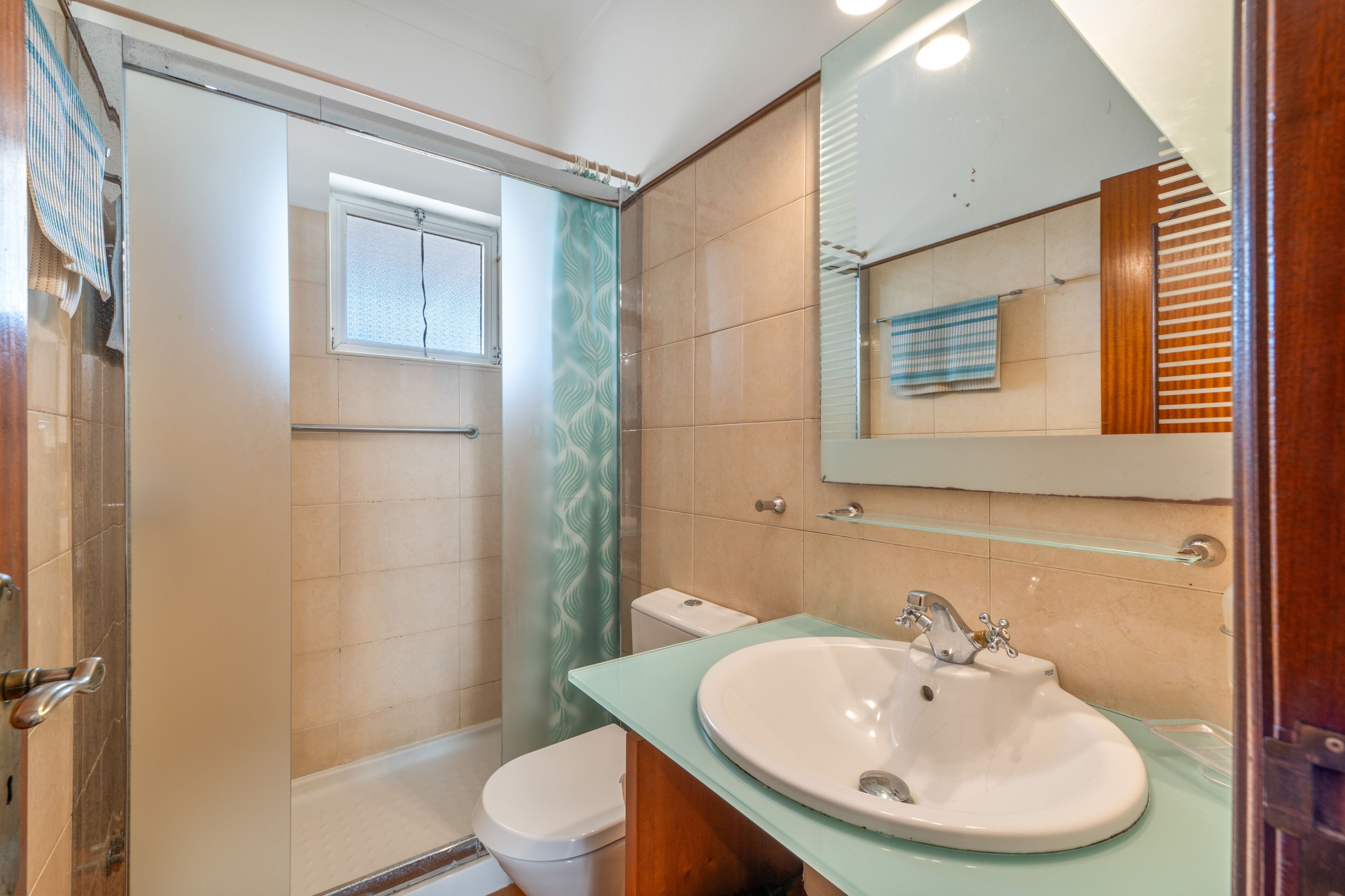 Een badkamer met een douchecabine van glas, een wit toilet, een wastafel met een glazen blad en een spiegel boven de wastafel.