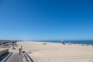 Una playa con un paseo marítimo de madera, sillas, sombrillas y una estación de salvavidas.