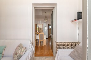A narrow hallway leading to a dining area with a table and chairs, a kitchen in the background, and a sofa with cushions on either side. - Holiday Home 'Encanto' with Private Terrace and Wi-Fi (Santo André)