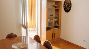 A dining area with a wooden table, chairs, a cabinet with dishes, and a window with curtains.