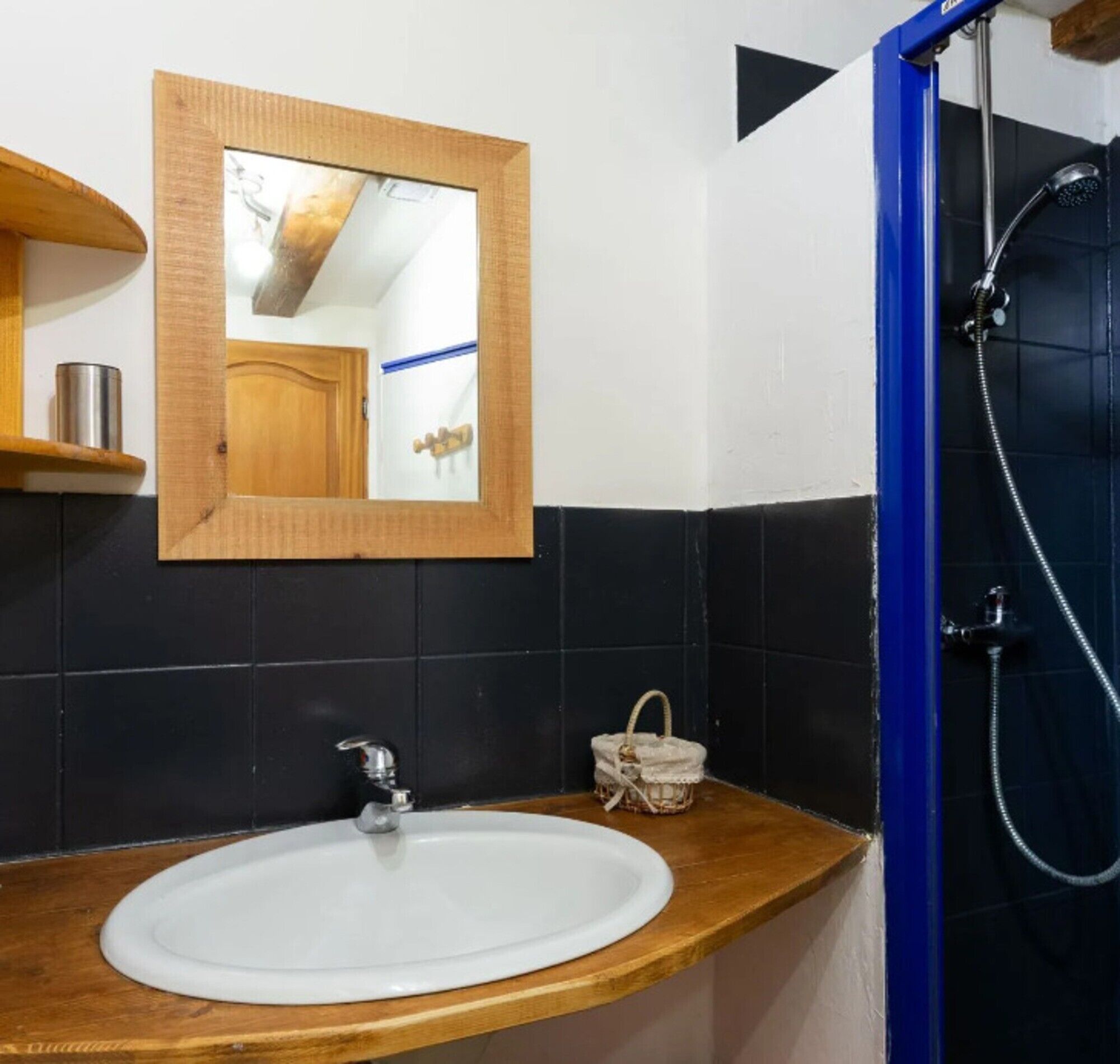 Un baño con tocador de madera, un lavabo blanco, un espejo, cabina de ducha y una pequeña cesta de mimbre.