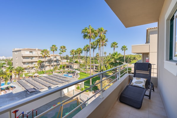 A balcony with a view of a pool, palm trees, and a building complex.
