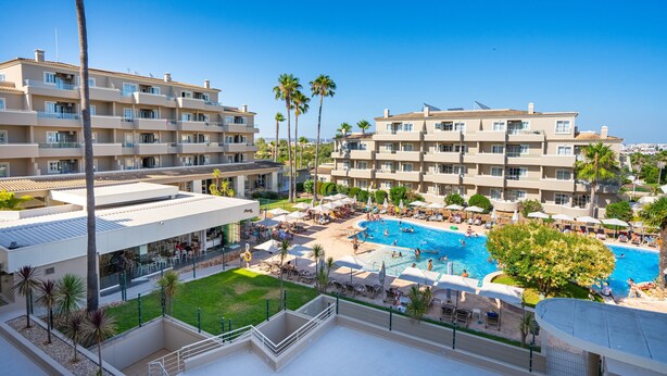 A hotel with multiple floors, a swimming pool, and palm trees.