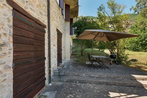 Un bâtiment en pierre avec une porte en bois, des places assises à l’extérieur et un espace barbecue.
