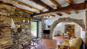 A rustic interior with stone walls, wooden beams, a stone fireplace, wicker chairs, a sofa, and a television. - Holiday Home 'Franca Nature Holidays' with Private Terrace, Private Garden and Wi-Fi (Rezzo)