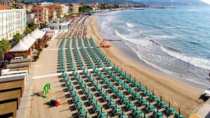 A beach with rows of green umbrellas and lounge chairs, a promenade with buildings, and a view of the sea and hills in the background. - Holiday Home 'Franca Nature Holidays' with Private Terrace, Private Garden and Wi-Fi (Rezzo)