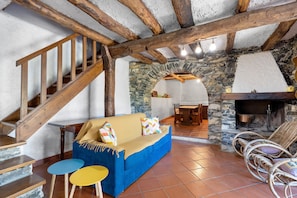 A rustic interior with a wooden staircase, a stone fireplace, a blue sofa, and wicker chairs. - Holiday Home 'Franca Nature Holidays' with Private Terrace, Private Garden and Wi-Fi (Rezzo)