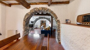A rustic interior with exposed wooden beams, a stone archway, a wooden dining table, and a vintage radio. - Holiday Home 'Franca Nature Holidays' with Private Terrace, Private Garden and Wi-Fi (Rezzo)