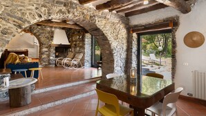 A rustic interior with stone walls, a wooden ceiling, a dining table with chairs, and a view through an open door. - Holiday Home 'Franca Nature Holidays' with Private Terrace, Private Garden and Wi-Fi (Rezzo)