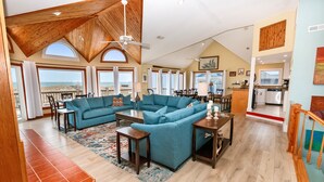 A spacious living area with a large blue sectional sofa, wooden flooring, and a view of the beach. - OCEANFRONT, wild horses, private pool, hot tub-4x2275, Over at Carova (Carova Beach)