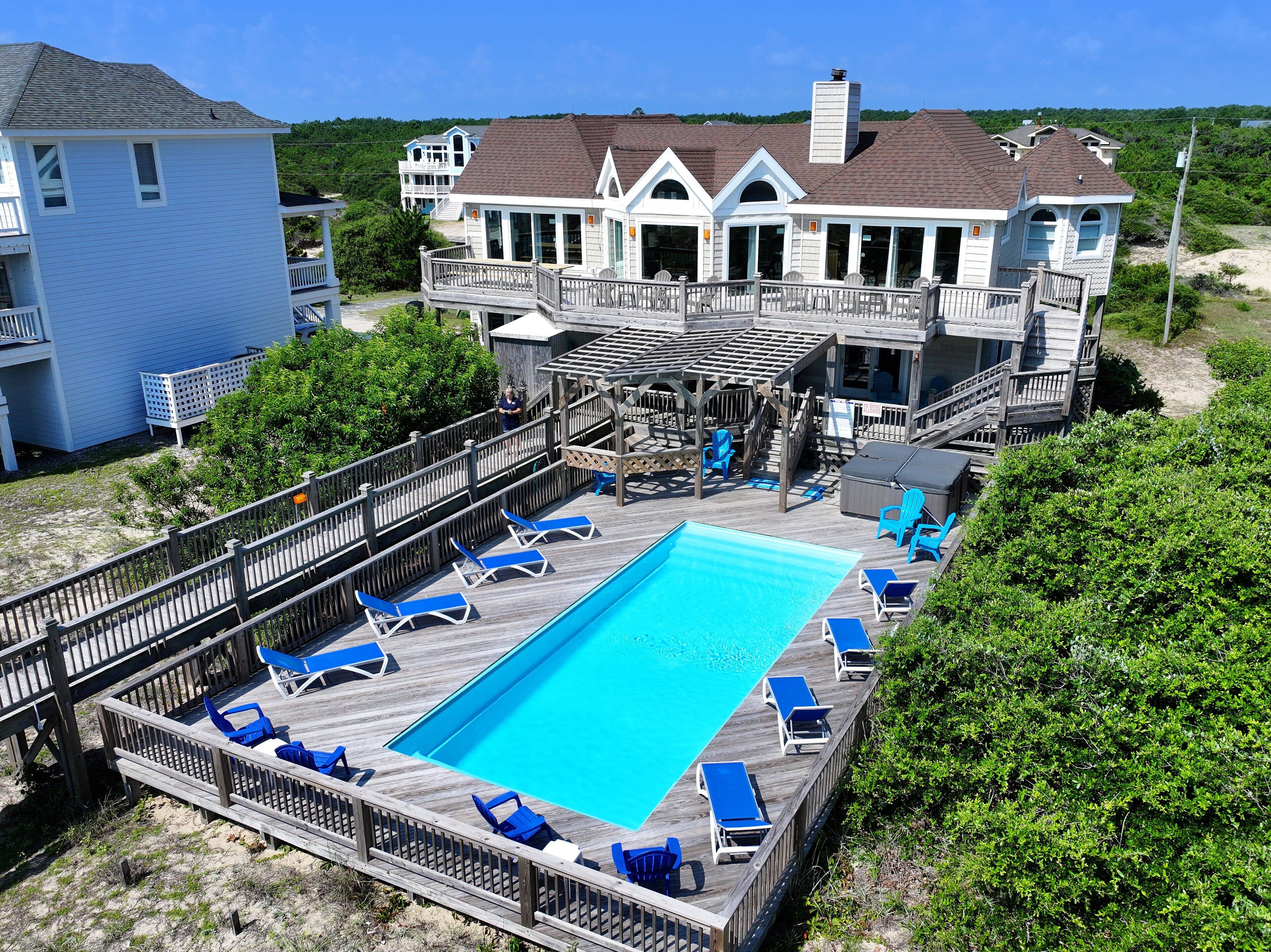 Une grande maison avec une piscine, des chaises longues et une terrasse en bois.