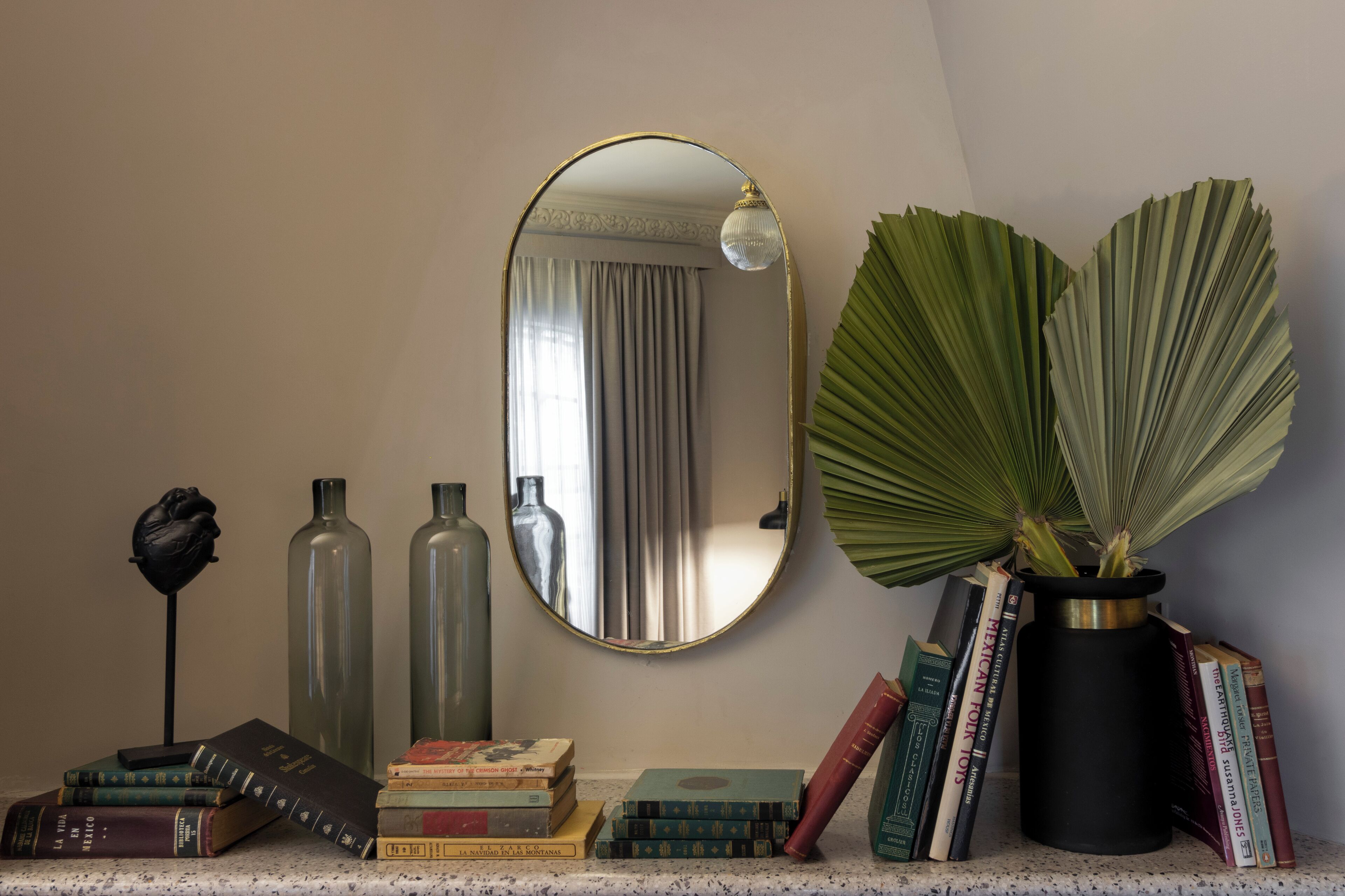 Une pièce avec un miroir, des livres, des vases décoratifs et une plante en pot.