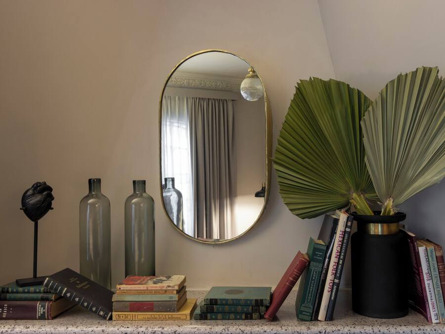 Une pièce avec un miroir, des livres, des vases décoratifs et une plante en pot.
