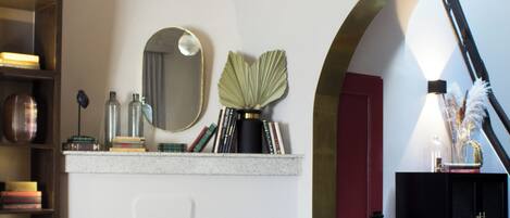 Een woonkamer met een open haard, boekenkasten, een spiegel en een rode deur.