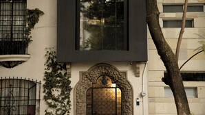 A building facade with a large window, a decorative door with a number plaque, and a tree in the foreground.