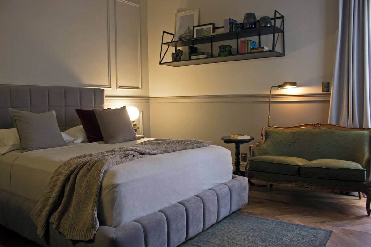 Ein ordentlich eingerichtetes Schlafzimmer mit einem großen Bett, einem grünen Sessel und einem Nachttisch.
