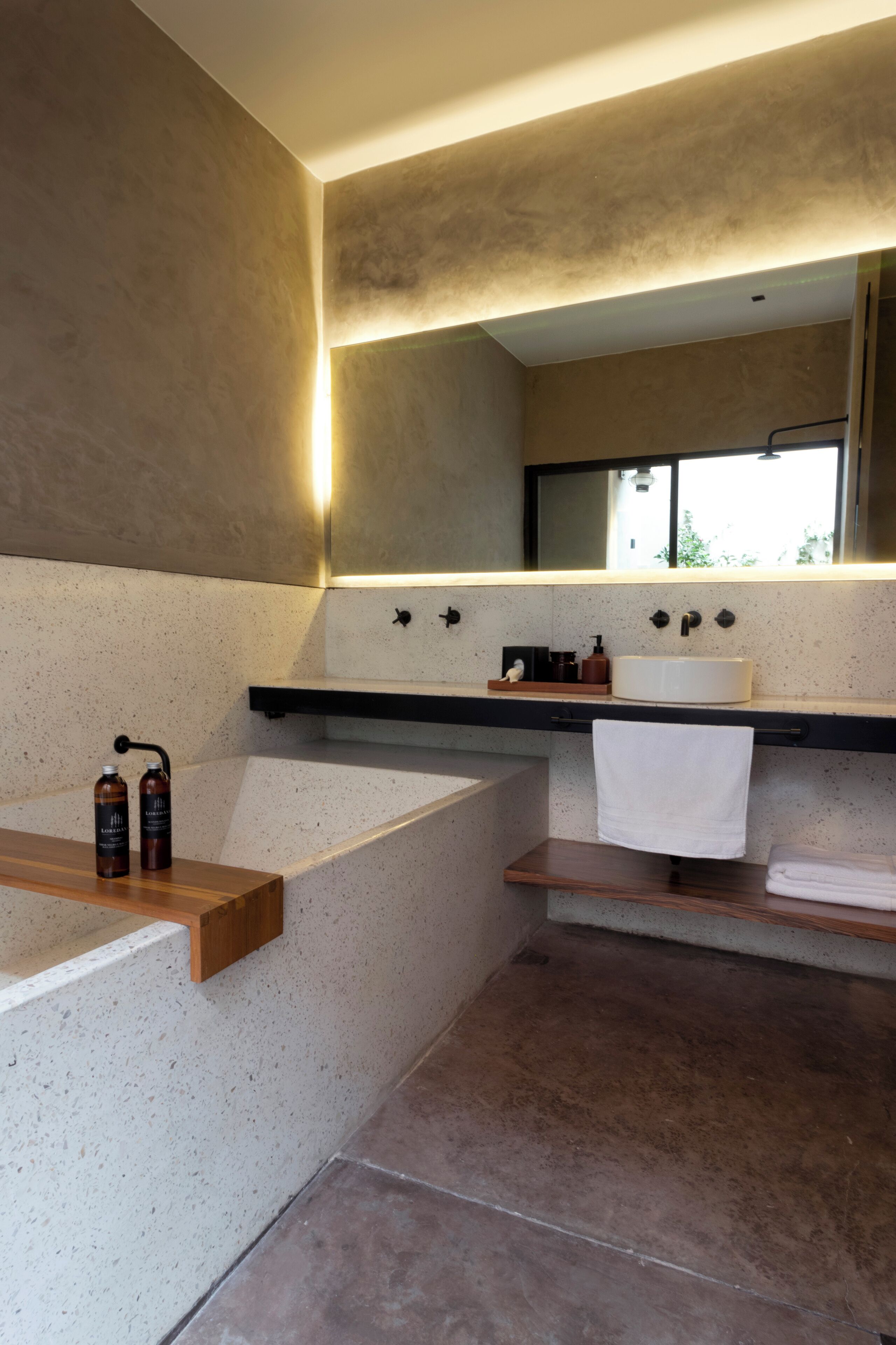 Ein modernes Badezimmer mit einer freistehenden Badewanne, einem großen Spiegel und einem hölzernen Ablagebrett mit Pflegeprodukten.