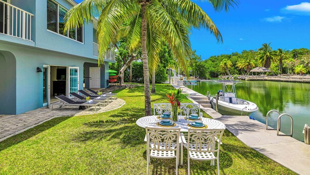 A two-story building with a pool, a boat dock, and a table set for dining. - Waterfront / Ocean Access Canal / Kamp Key / Homes (Islamorada)