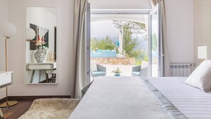 Une chambre d’hôtel avec un grand lit, un bureau doté d’un miroir et une vue sur un espace extérieur aménagé avec des sièges.