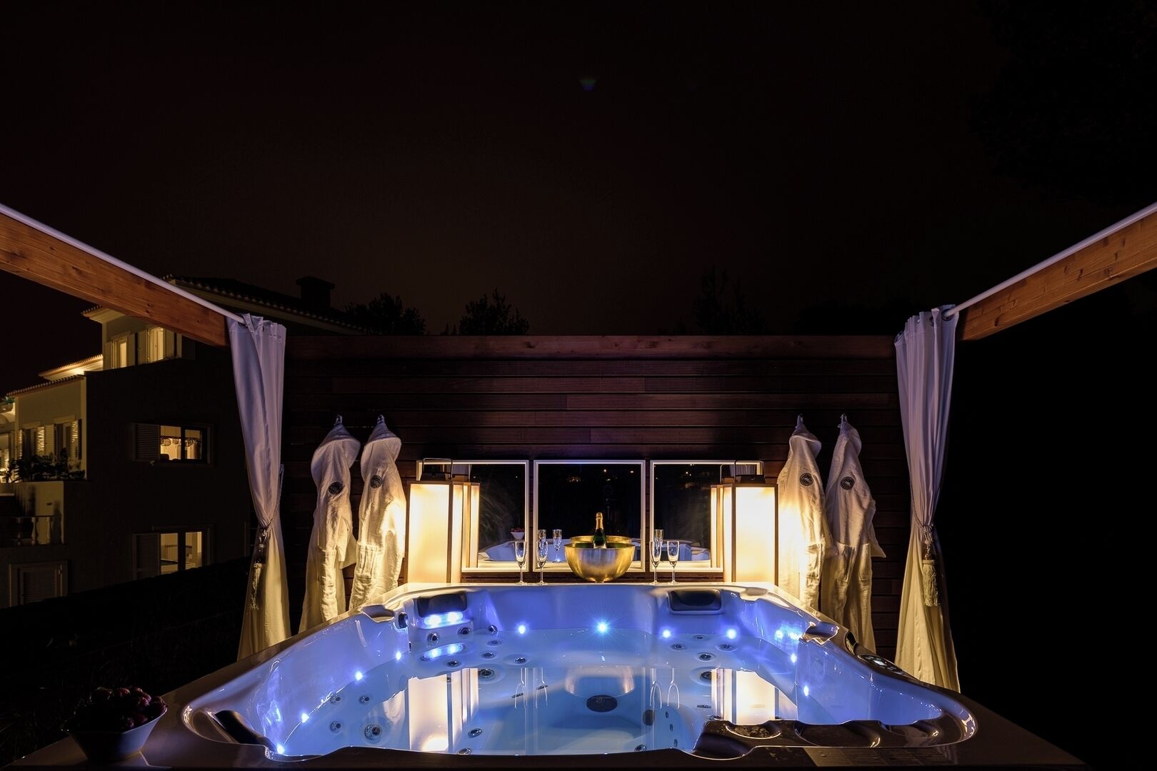 A hot tub with a wooden deck and a view of a building in the background.