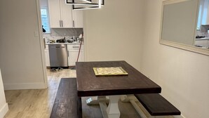 A dining area with a wooden table and benches, a modern pendant light, and a kitchen in the background. - Dive In! The Poolside Escape with a Hot Tub, Grill, Game Room & Good Times. (Lewisville)