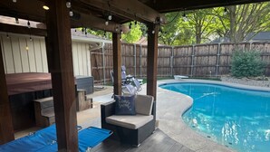 A covered outdoor area with a pool, wooden deck, and seating. - Dive In! The Poolside Escape with a Hot Tub, Grill, Game Room & Good Times. (Lewisville)