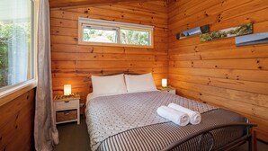 Een slaapkamer in een houten blokhut, met een bed, bedlampen en een raam.