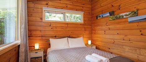 Ein Schlafzimmer einer Holzhütte mit einem Bett, Nachttischlampen und einem Fenster.