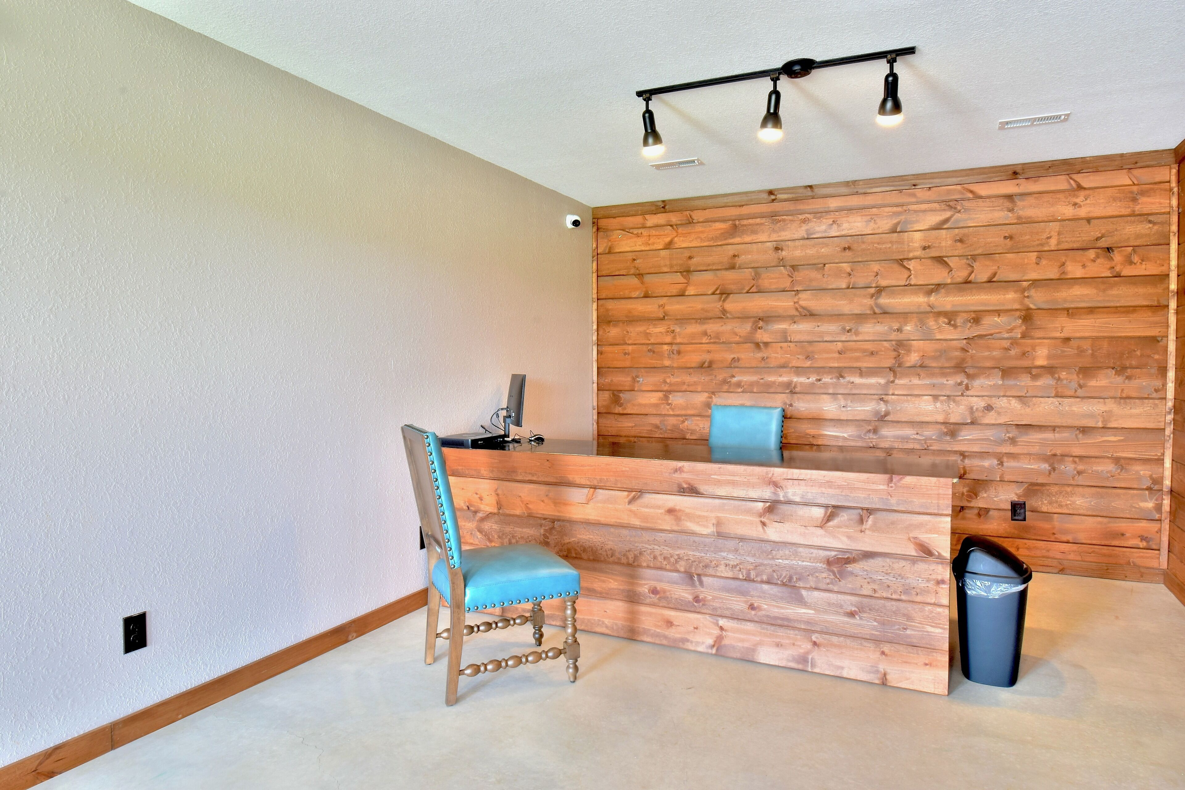 A reception area with a wooden wall, a blue cushioned chair, and a trash bin.