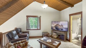 Een gezellige loft slaapkamer met een schuine plafond, een groot raam, een televisie en een badkamer die door een open deur zichtbaar is.
